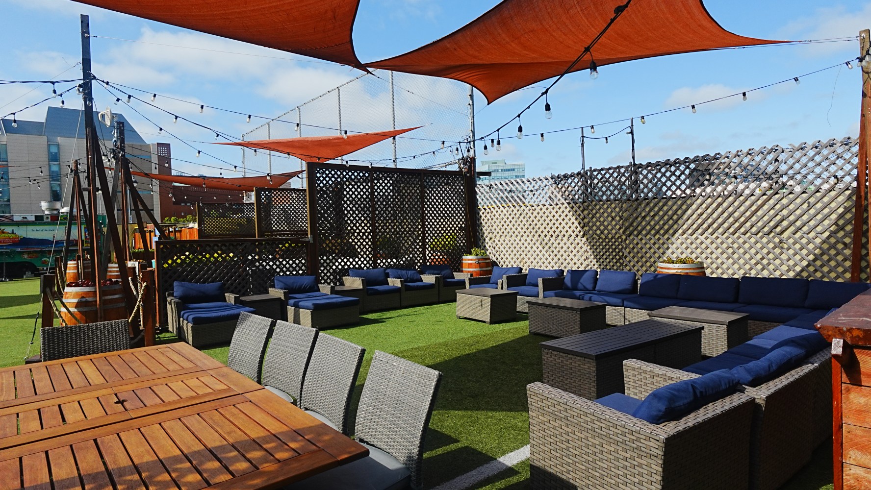 Outdoor patio with wooden tables, wicker chairs, and canopy shades.