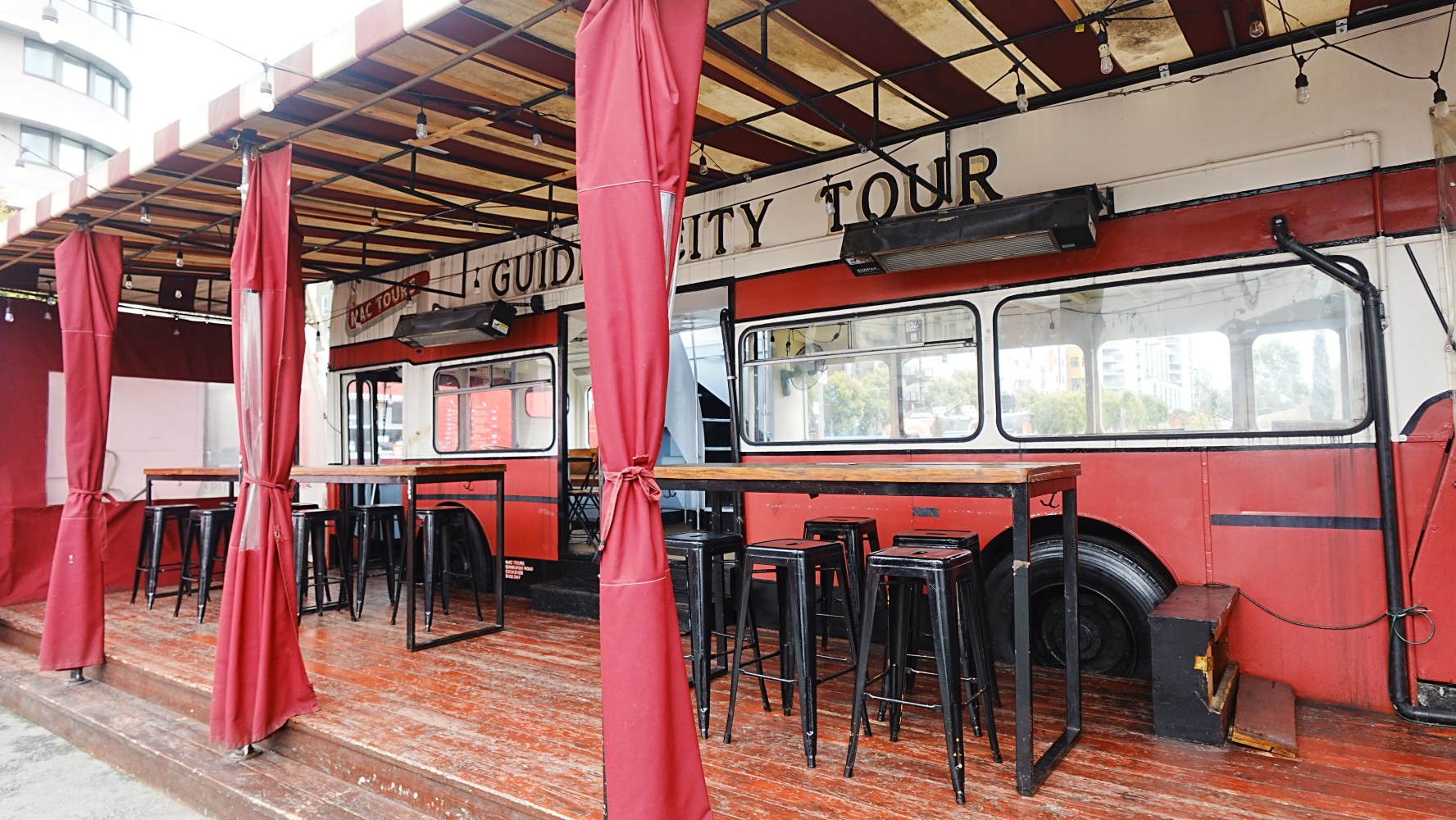 Open-air café with red canopy and a vintage bus inside.