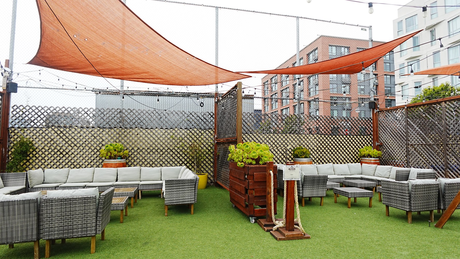 Outdoor lounge with gray wicker furniture, orange shades, and green turf.