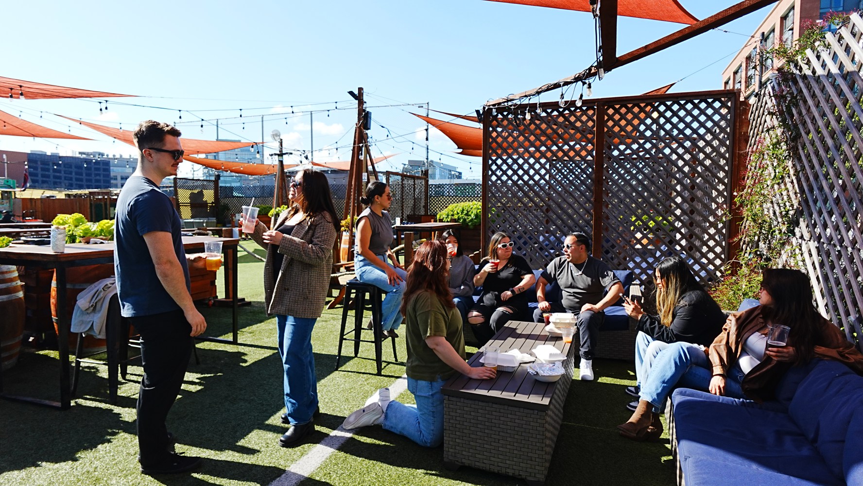 Group socializing on a sunny, outdoor patio with seating and shade sails.