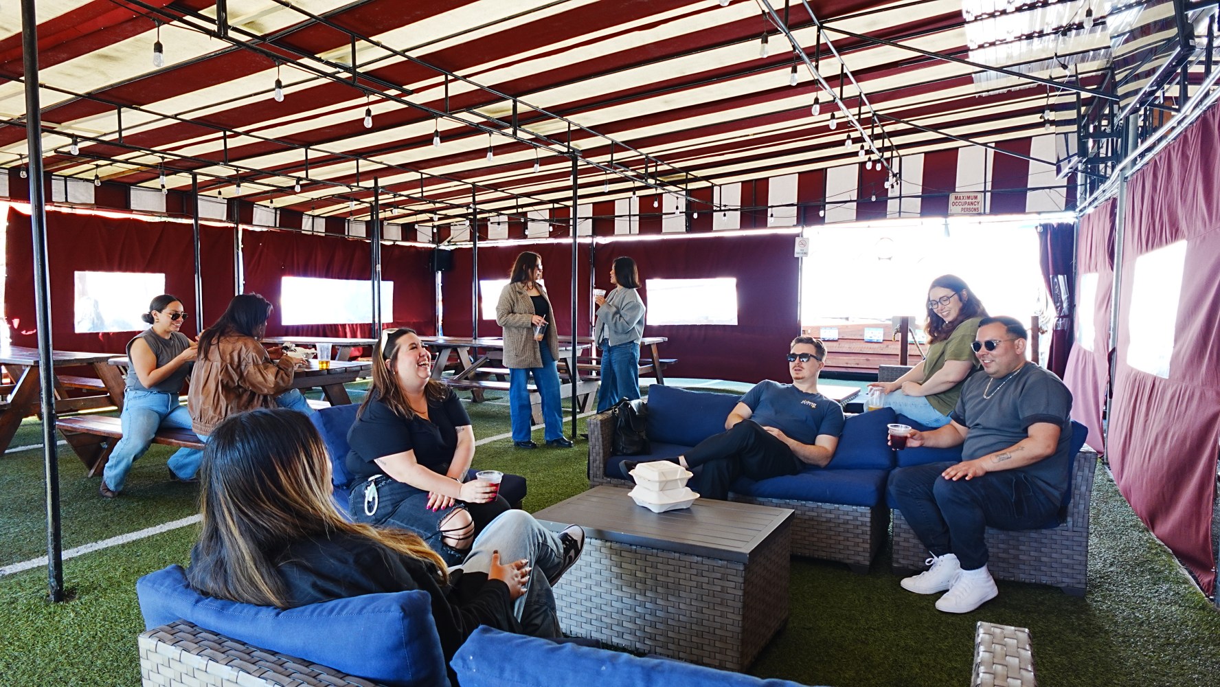 People sitting on sofas in a canopy-covered outdoor area with red and white striped roof.