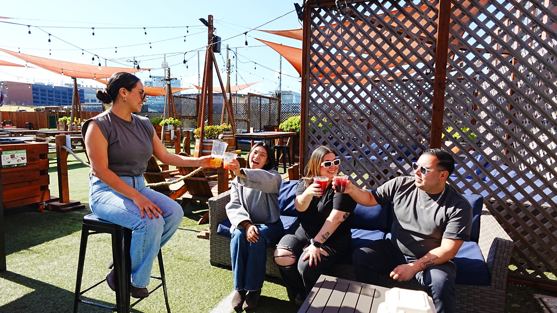Four people toasting drinks outdoors on a sunny patio.
