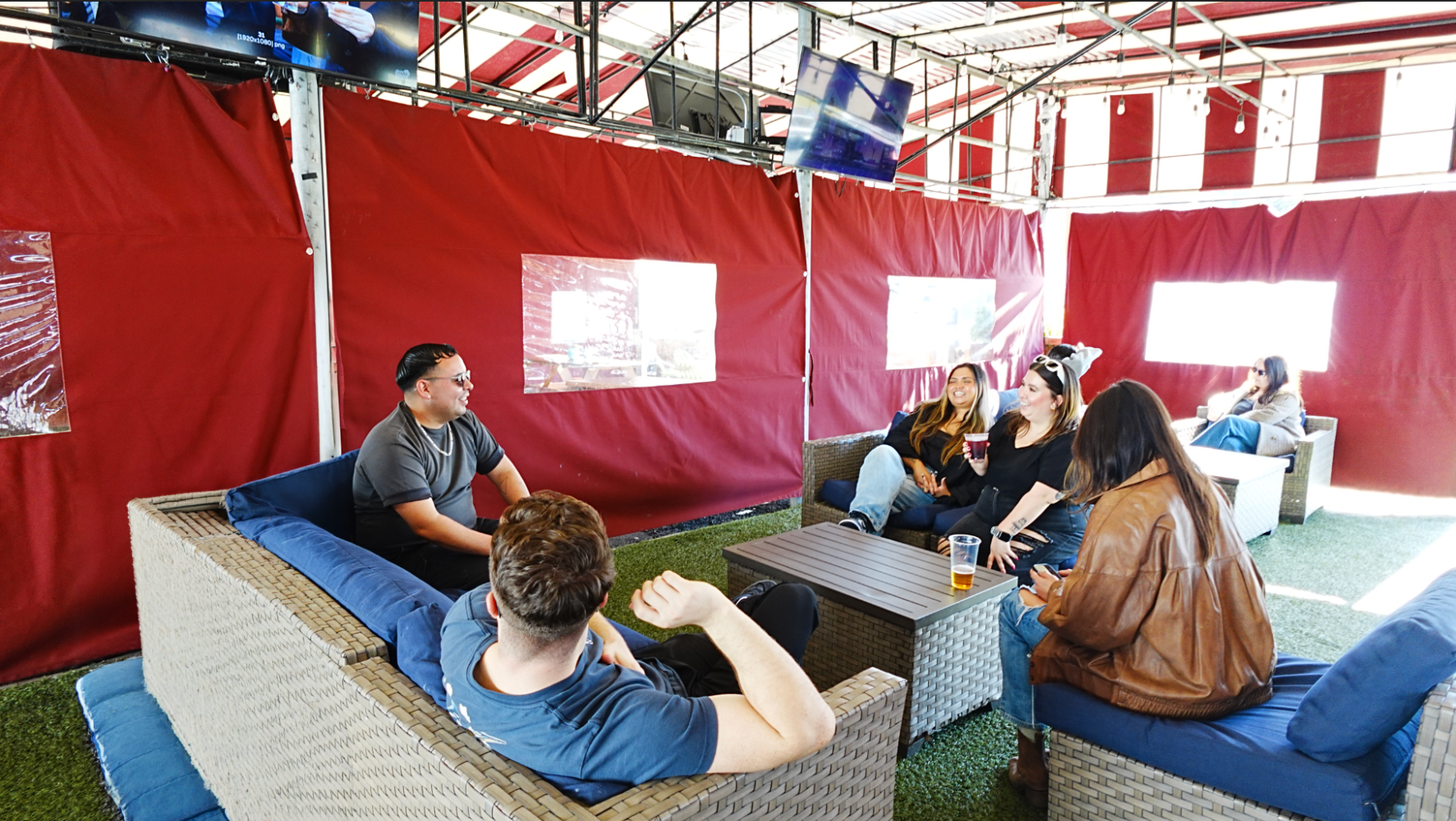 Group of people sitting on patio furniture under a red tent.