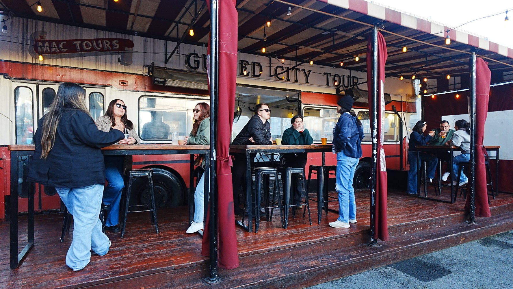 People socializing at an outdoor cafe with bus theme.