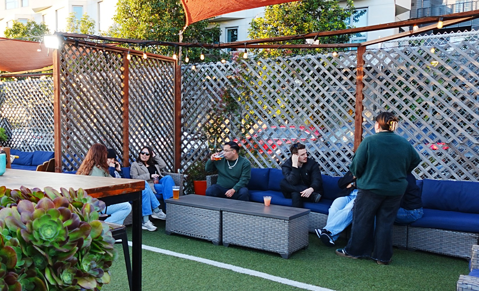 People sitting on a patio with sofas and lattice walls, under string lights.