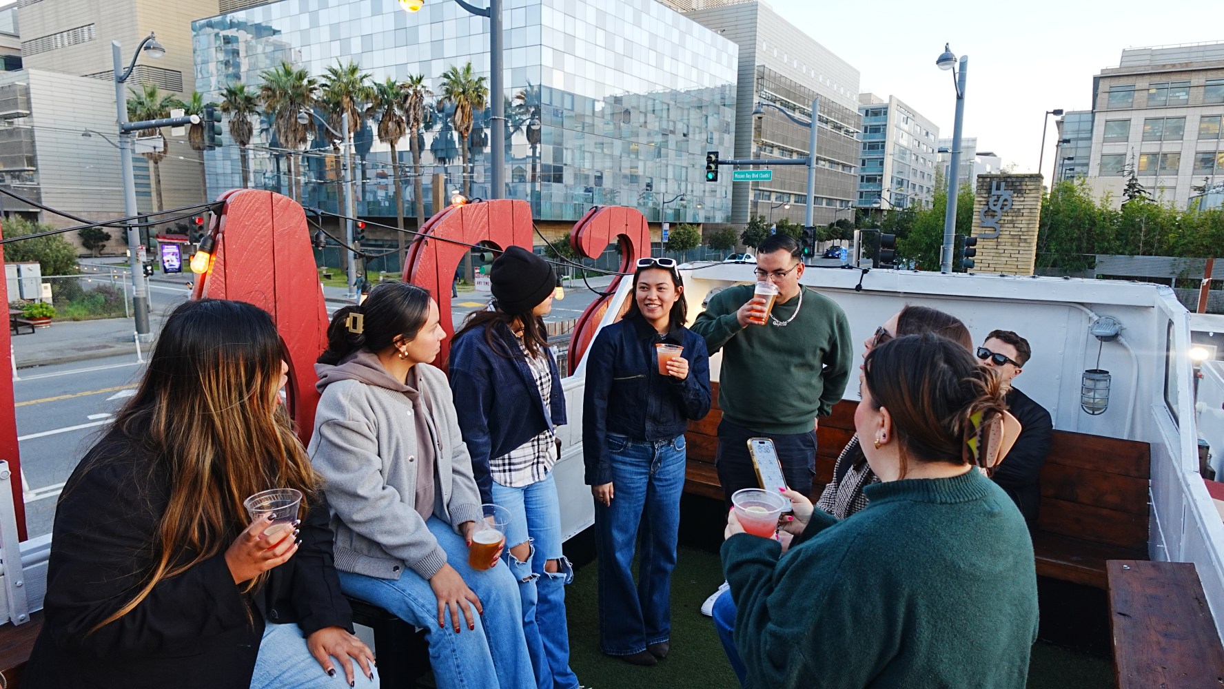 Group of people socializing on a rooftop with drinks, city buildings in the background.