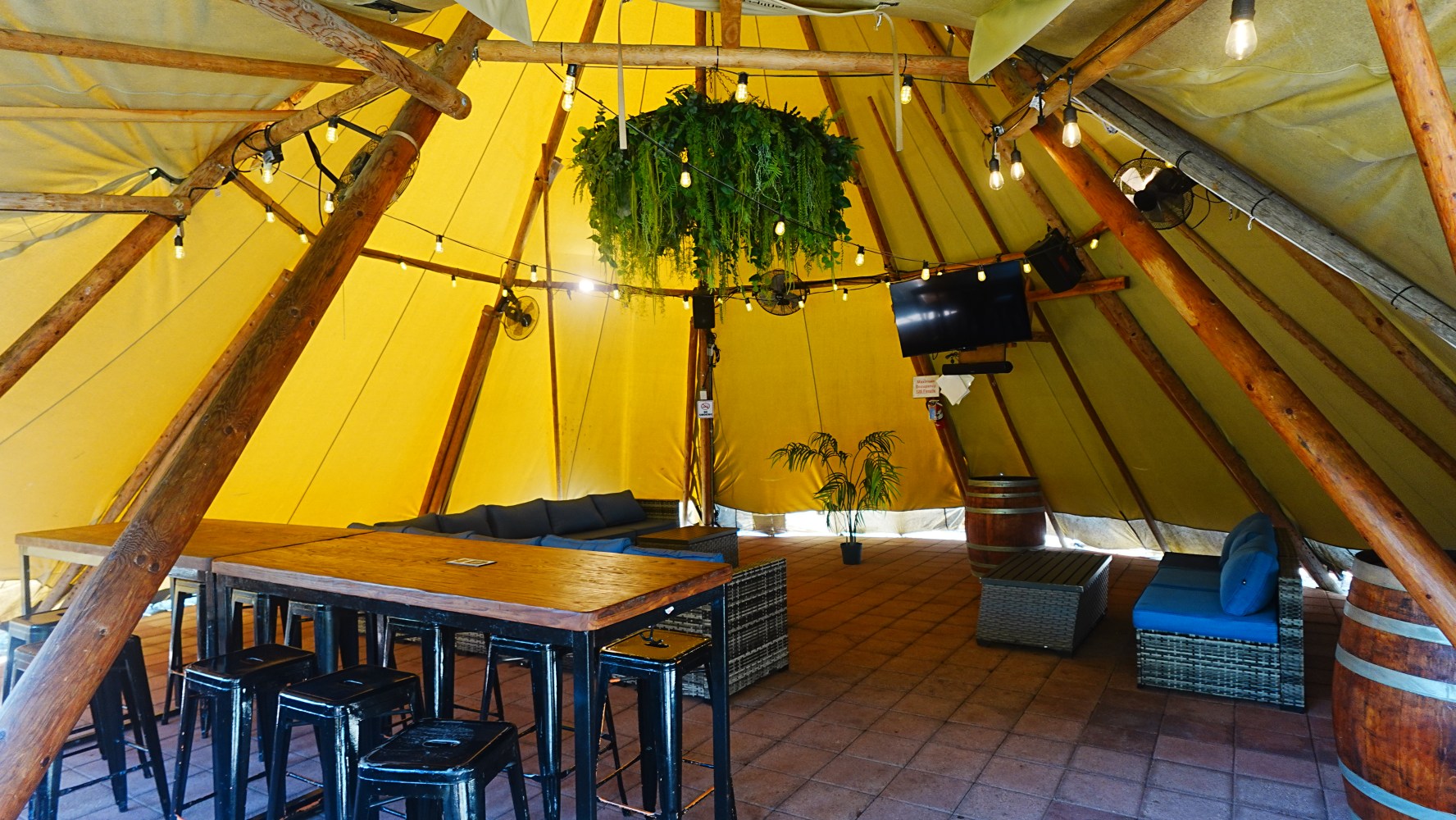 Inside view of a tent with seating, tables, plants, and a TV.