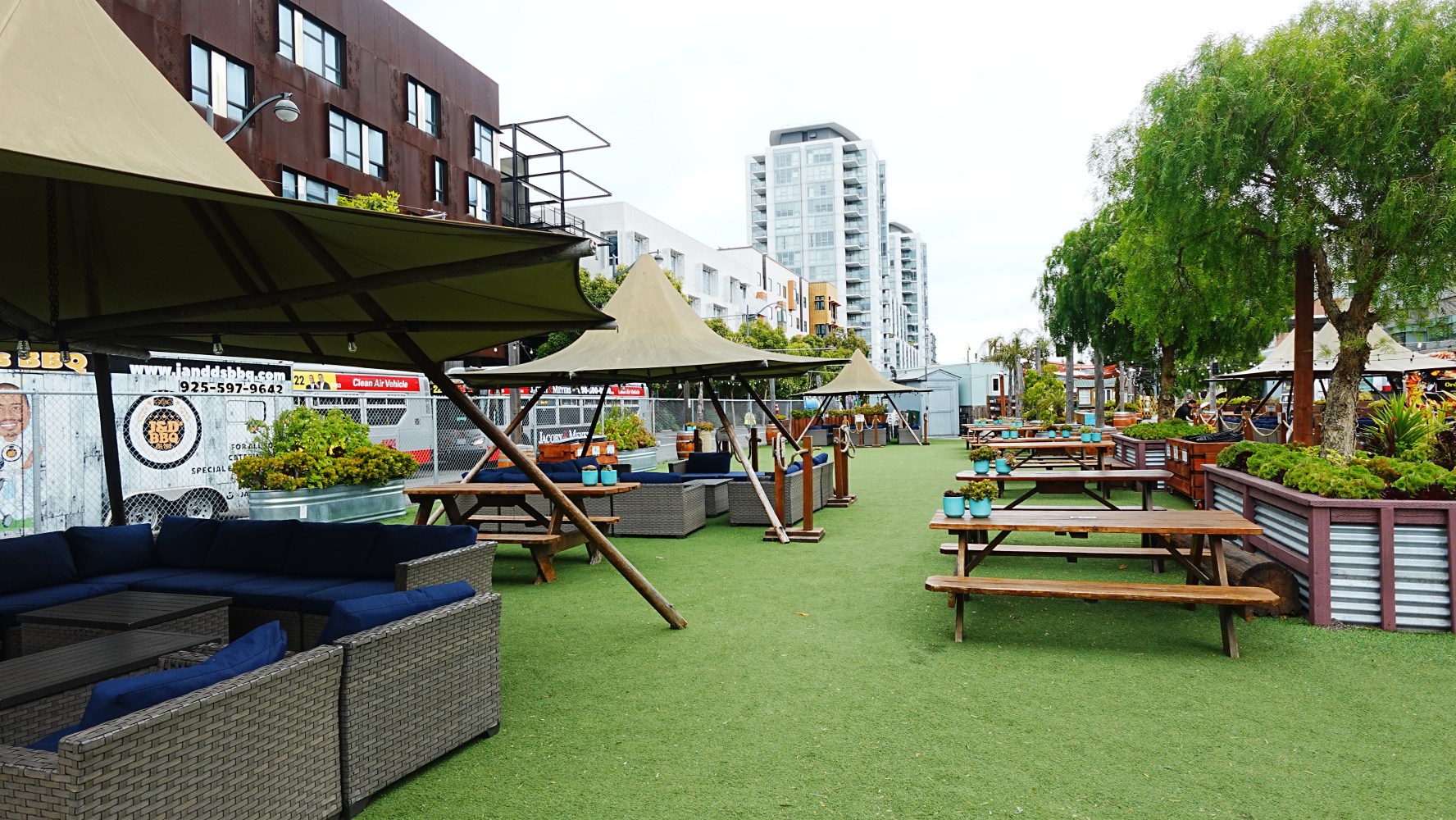 Outdoor seating area with wooden tables and large umbrellas on artificial grass.