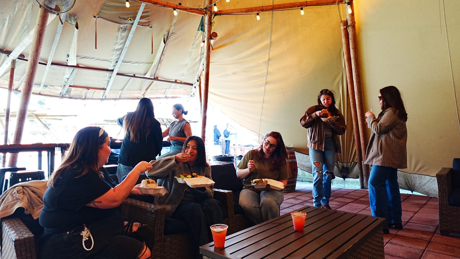 People eating and talking in a cozy, tented outdoor setting.