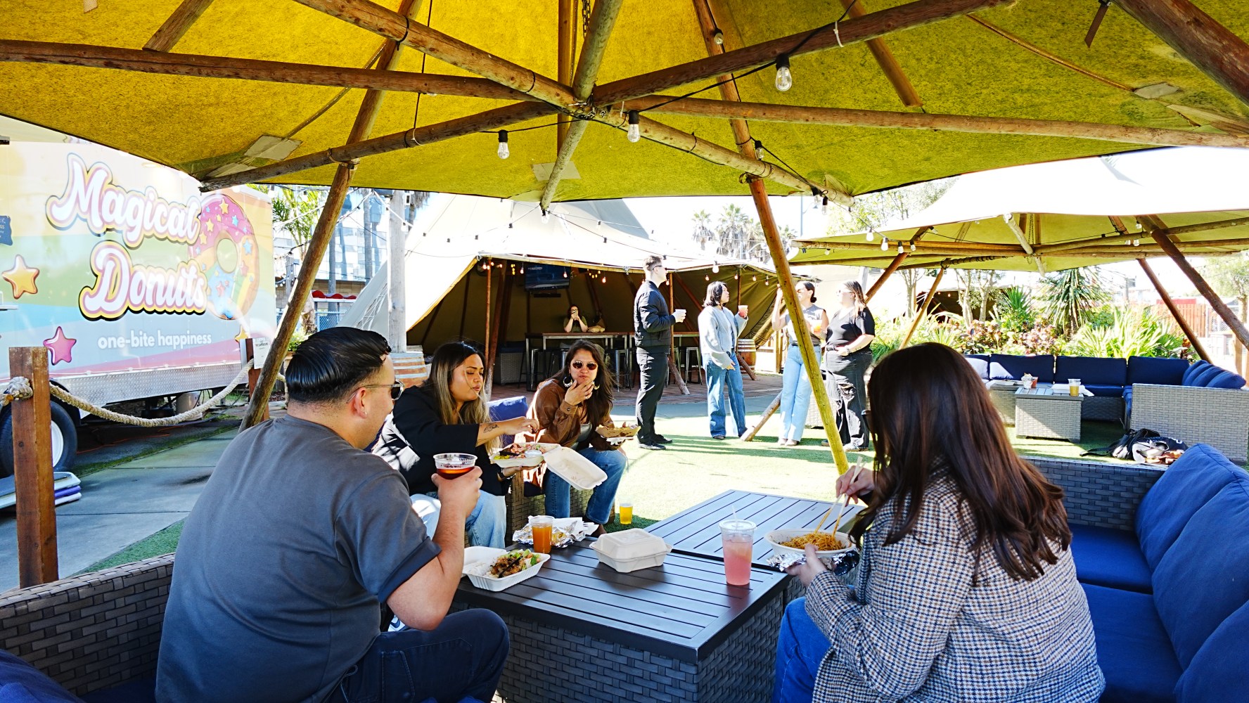 People dining outdoors under yellow canopies near a food truck.