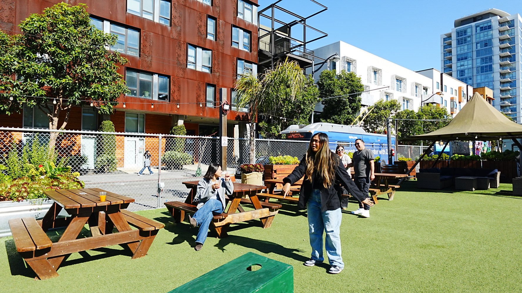 People enjoying a sunny day in a city park with benches and buildings nearby.