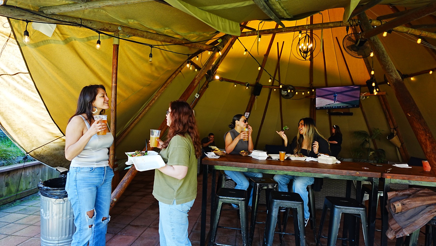 People socializing in a rustic tent with drinks at a bar table.