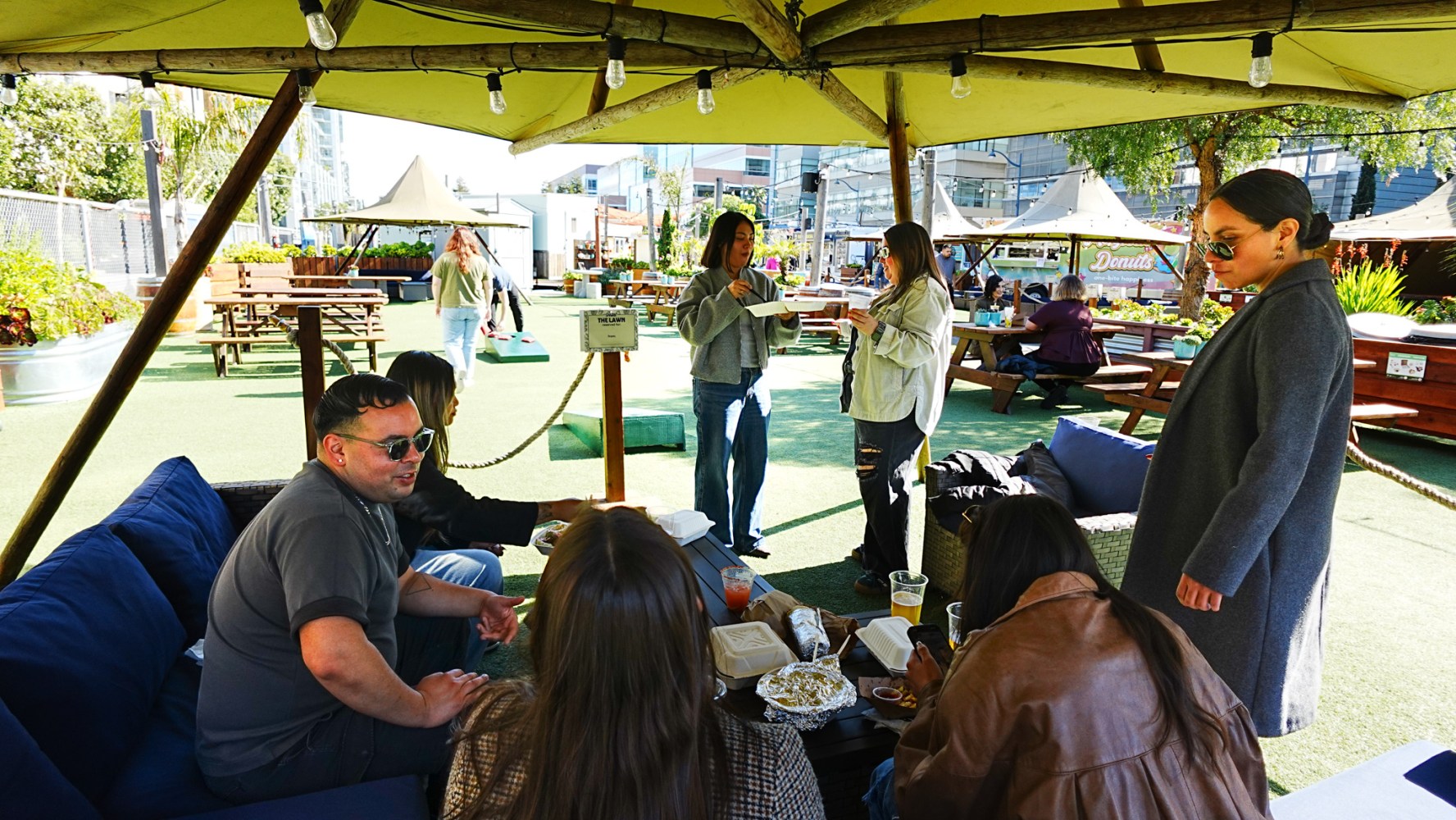 Group of people socializing at outdoor seating area with tables.