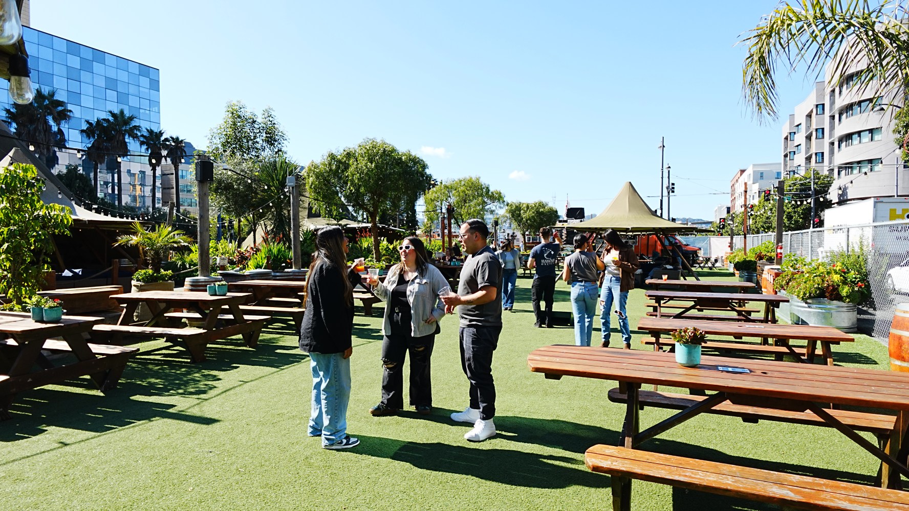 People talking in an outdoor area with picnic tables and palm trees.