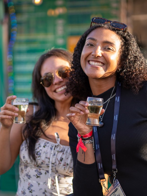 Two women smiling and holding drinks at an outdoor event.