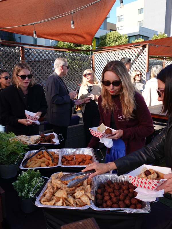 People at an outdoor gathering serving themselves food from trays under shade canopies.