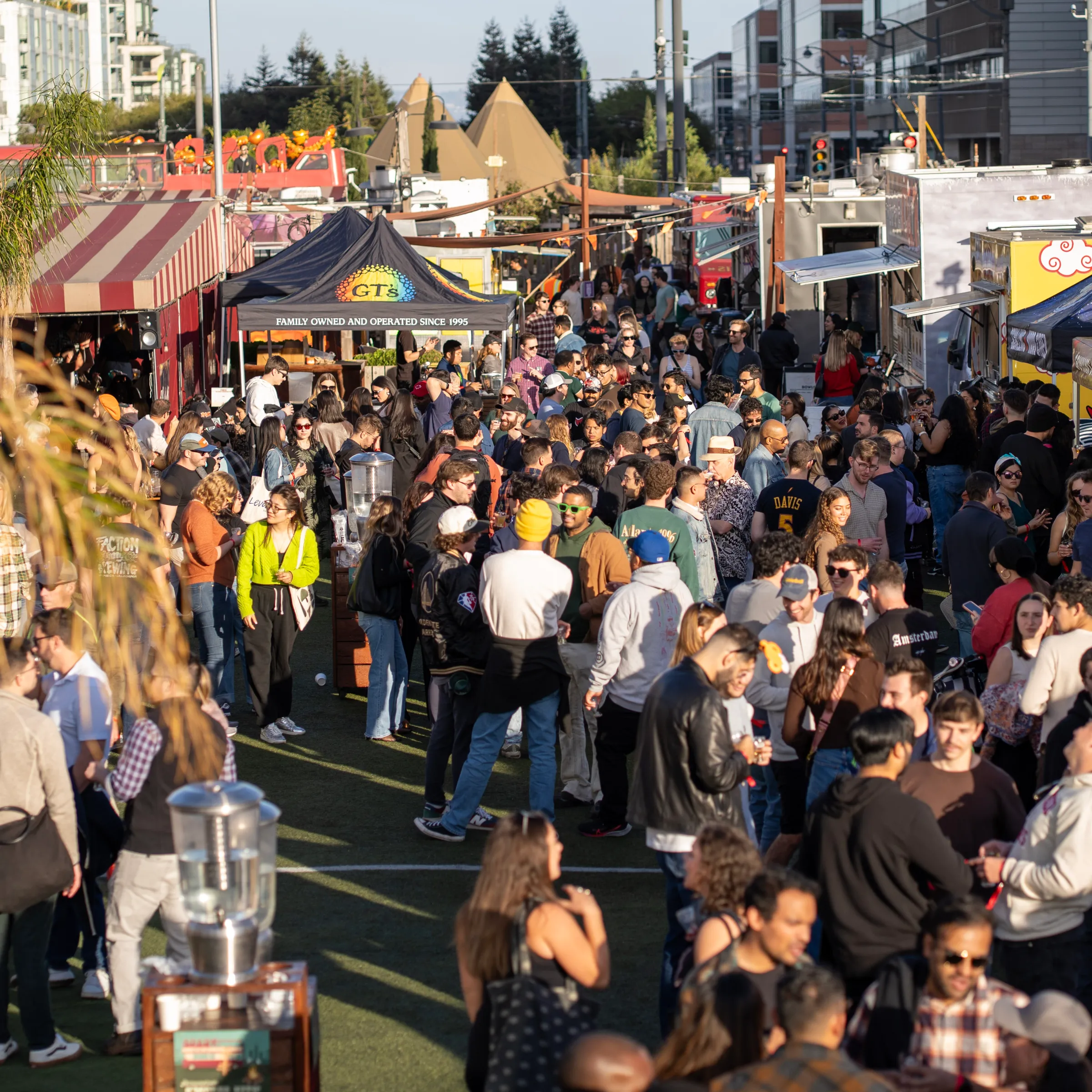 Crowded outdoor festival with many people near food trucks and tents on a sunny day.