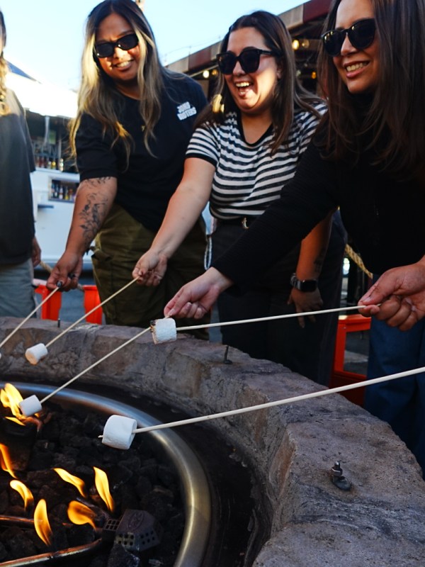 Group of people roasting marshmallows over a fire pit outdoors.