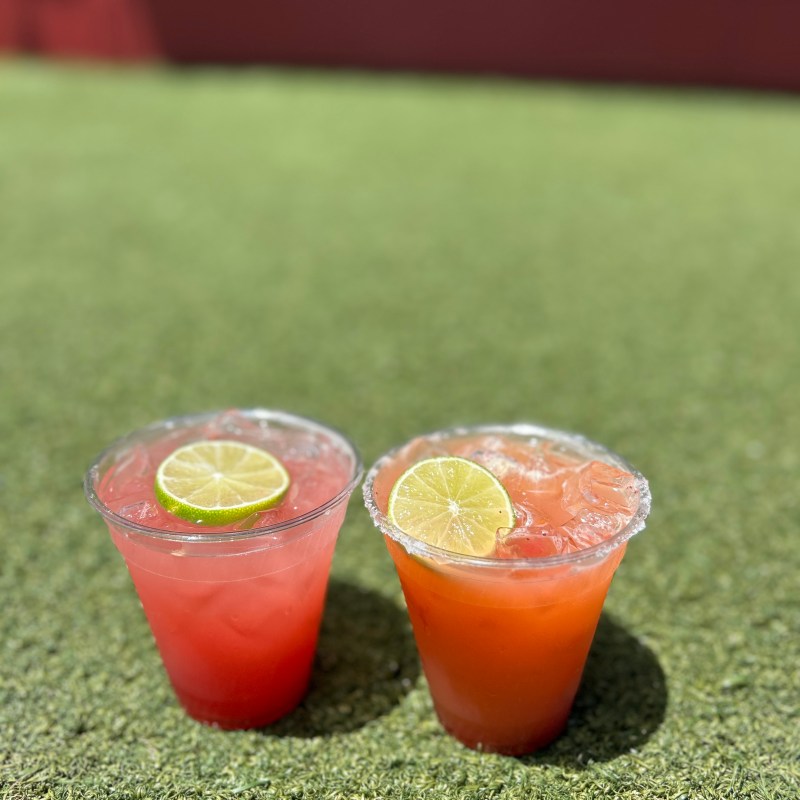 Two colorful drinks with lime slices on artificial grass, sunny setting.