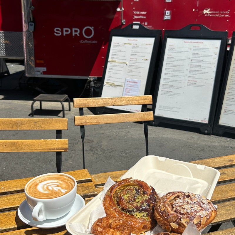 Coffee and pastries on a wooden table in front of a red food truck.