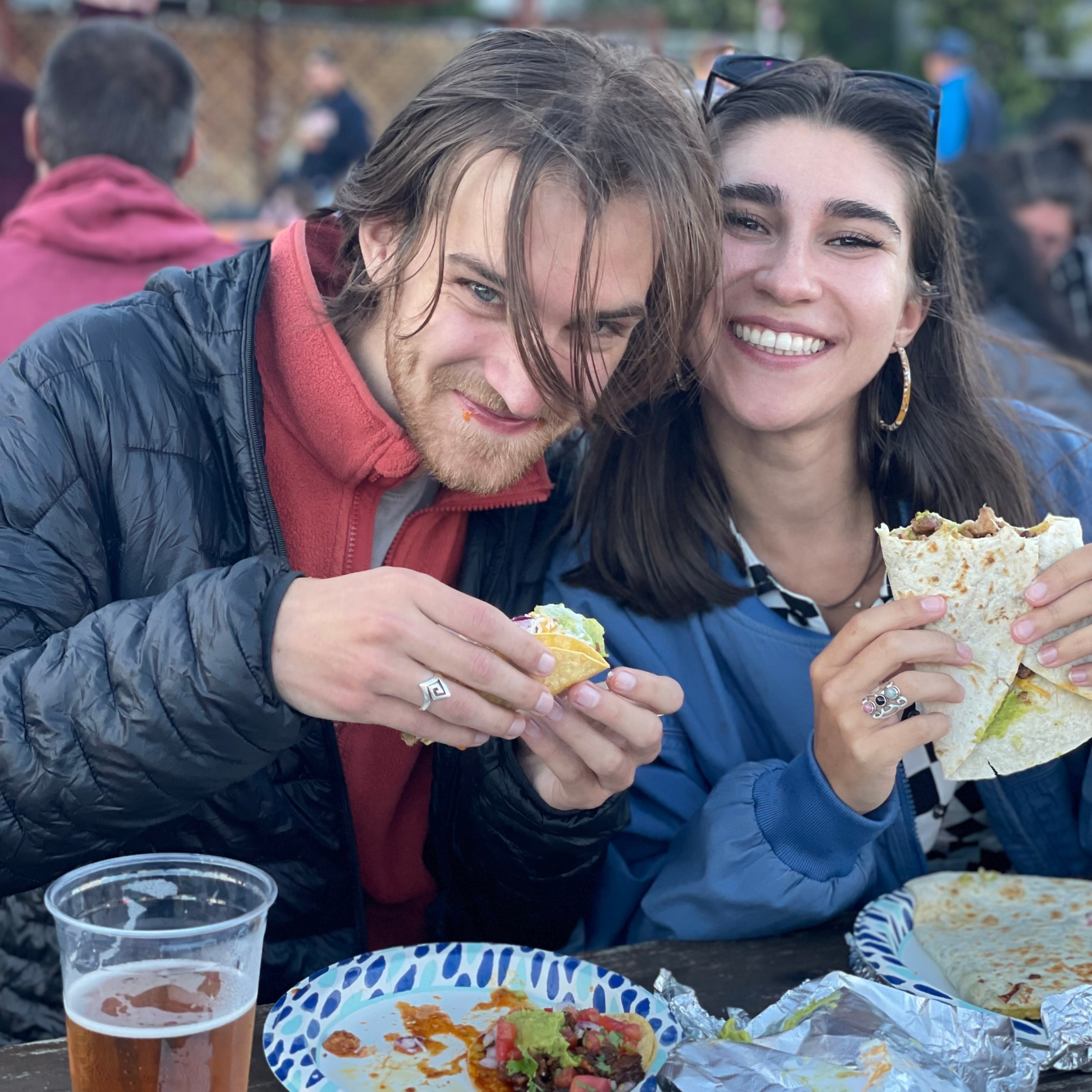 Smiling couple enjoying tacos and drinks at an outdoor table.