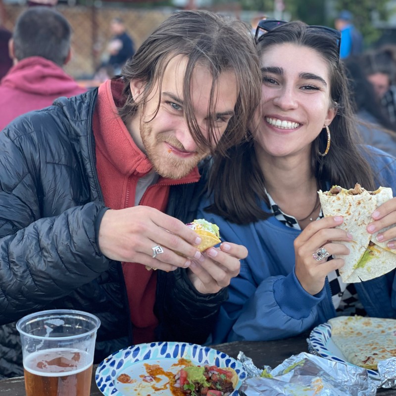 Smiling couple enjoying tacos and drinks at an outdoor table.
