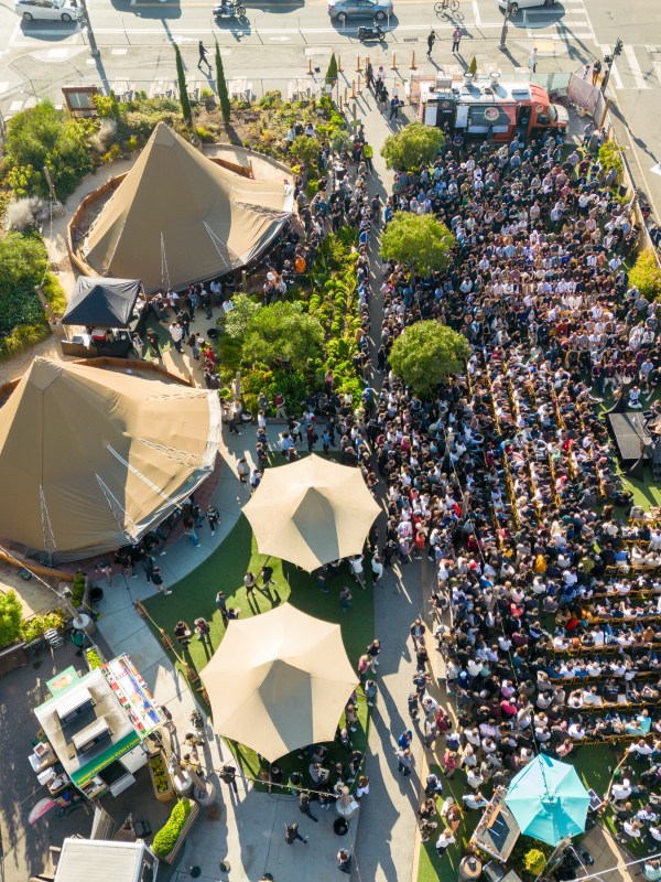 Aerial view of an outdoor event with two large tents and a seated crowd.