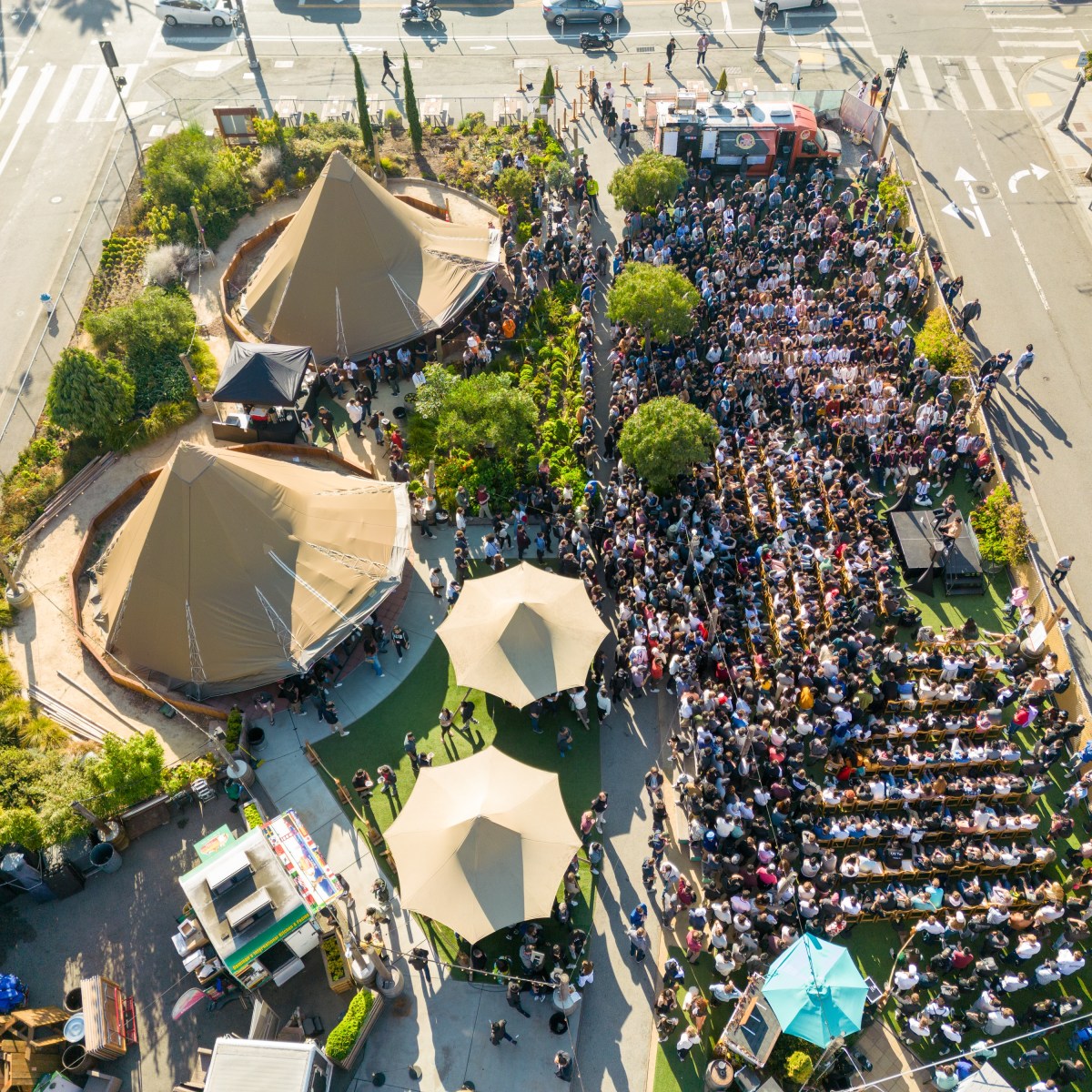 Aerial view of an outdoor event with two large tents and a seated crowd.