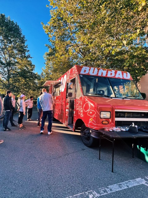 People standing in line at a red food truck named Bunbao on a sunny day.