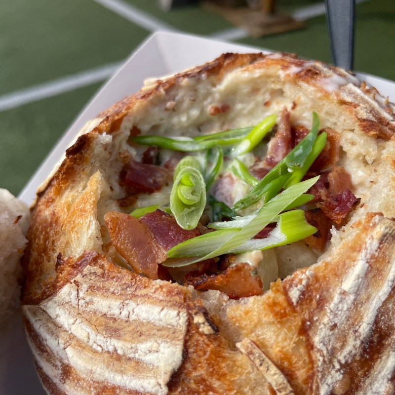 Bread bowl filled with soup, bacon, and green onions on a tray.