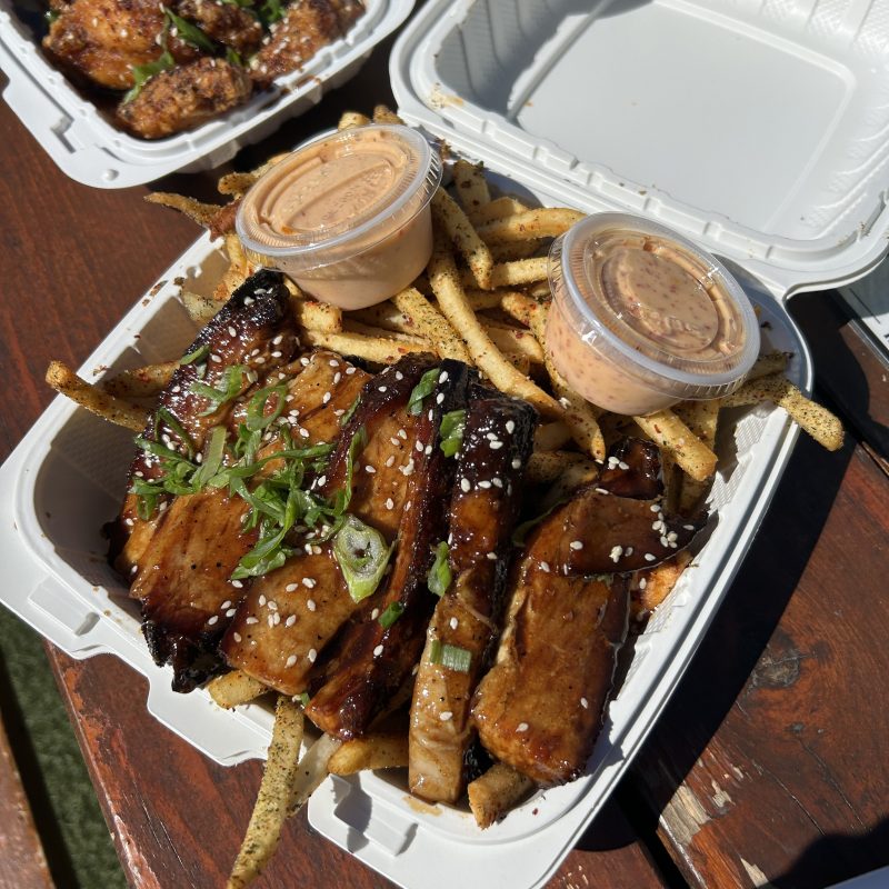 Grilled ribs and seasoned fries in a box with two sauce cups.