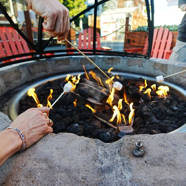 People roasting marshmallows over a fire pit with red chairs in the background.