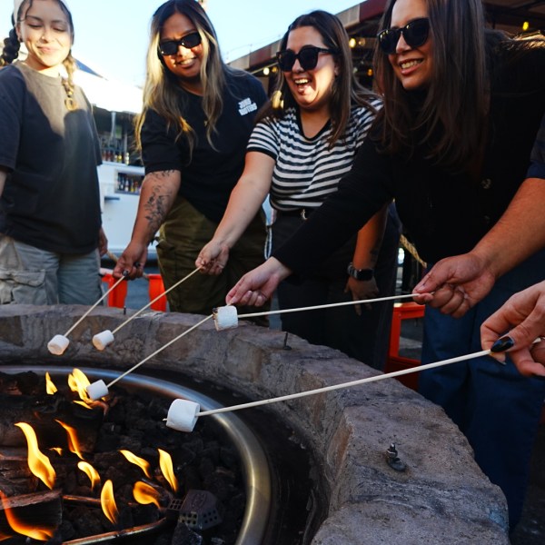 Five people roasting marshmallows over a fire pit, smiling and enjoying the activity.