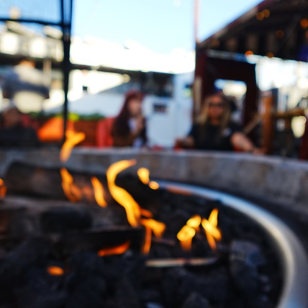 Blurred outdoor scene with a fire pit in focus and people in the background.