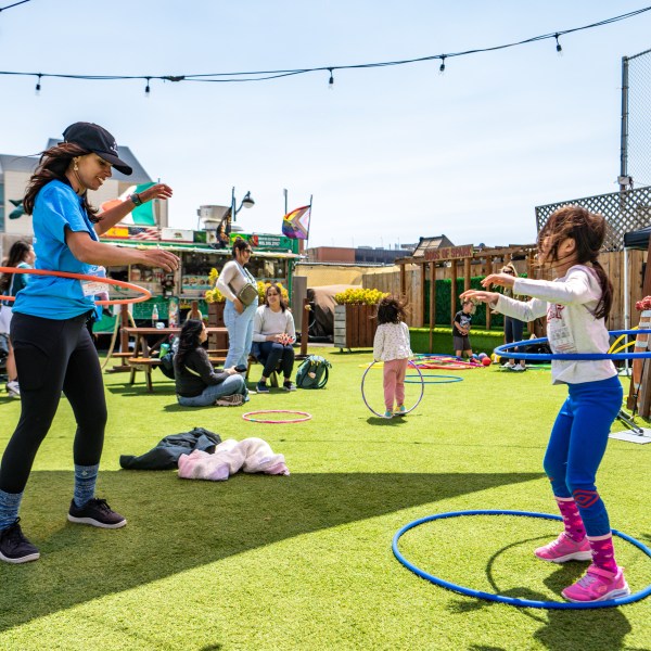 Adults and kids hula hooping on a grassy rooftop with urban background.