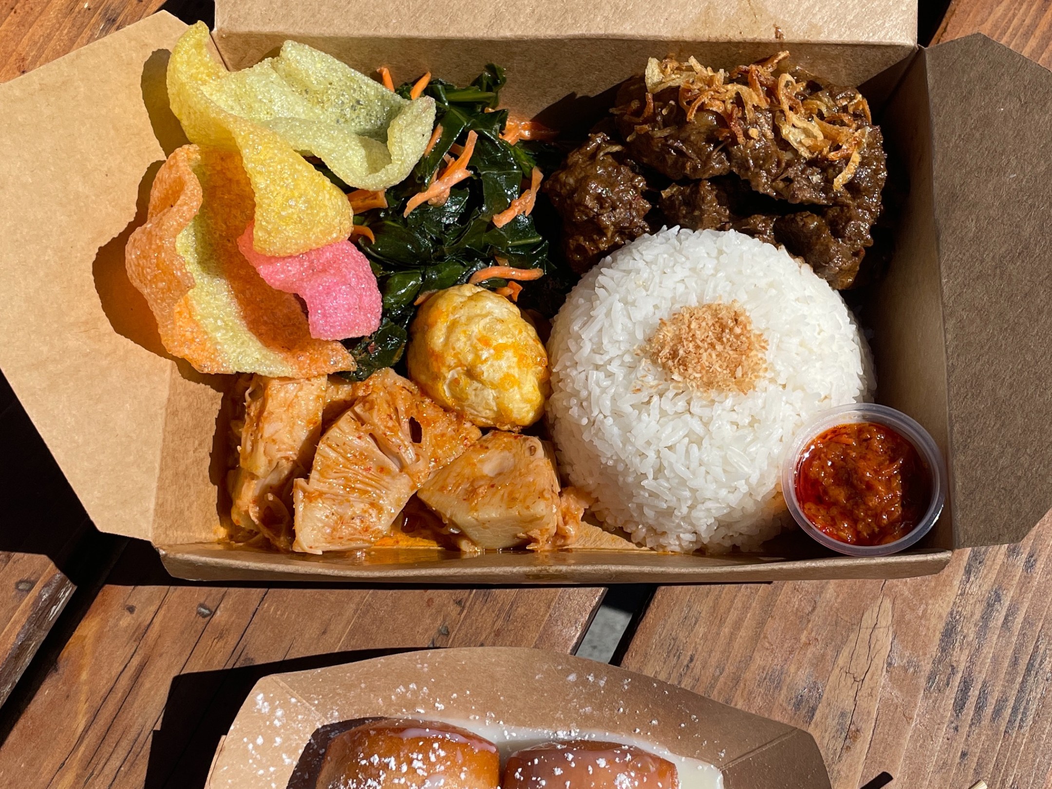 Boxed meal with rice, beef, veggies, pickles, chips; side of sugared donuts with dipping sauce.