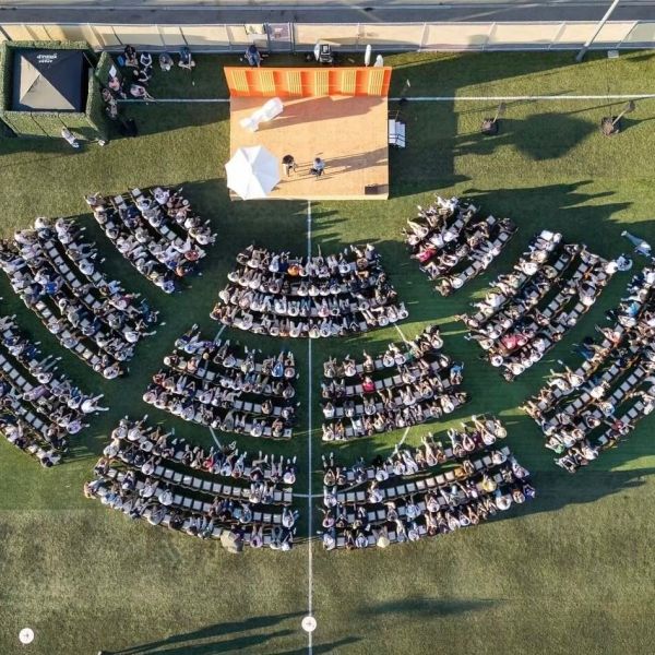 Aerial view of outdoor event with stage and audience seated in semicircles on grass.