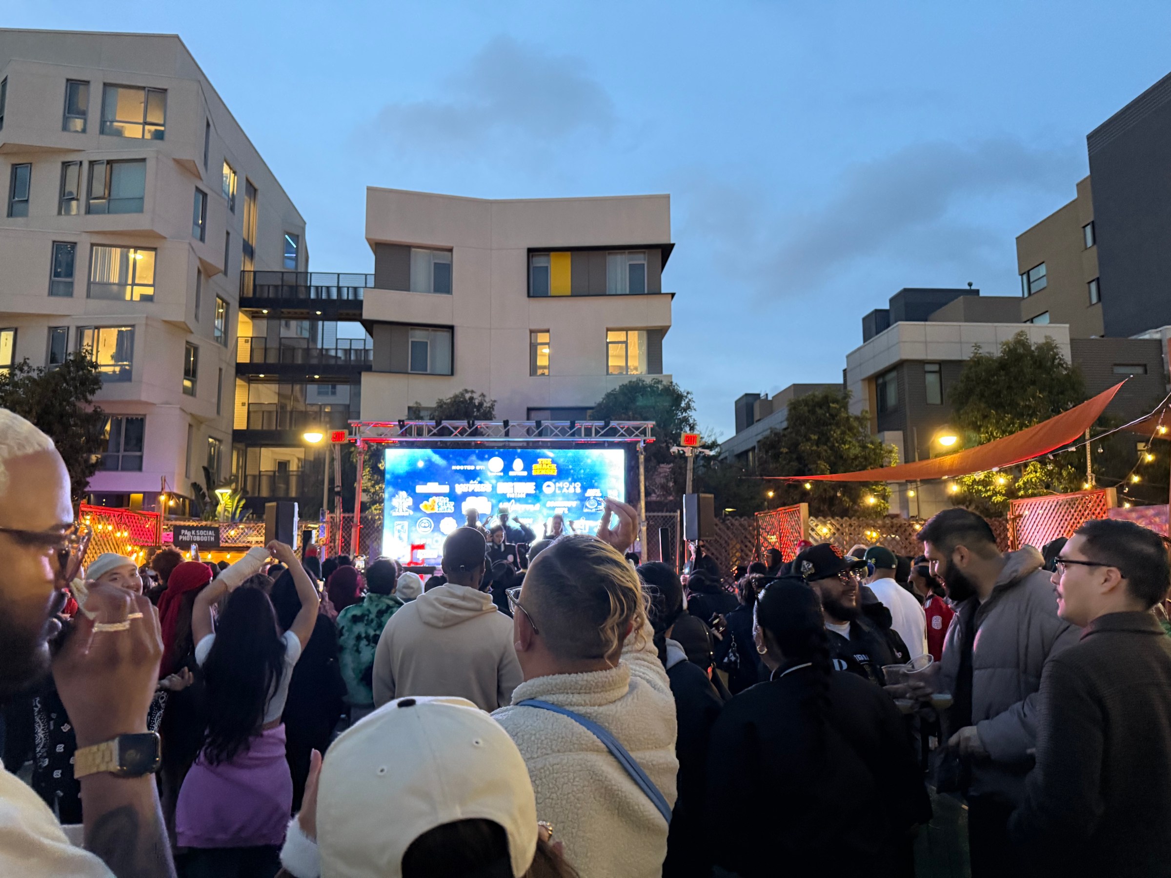 Crowd watching a performance on stage in a courtyard at dusk.