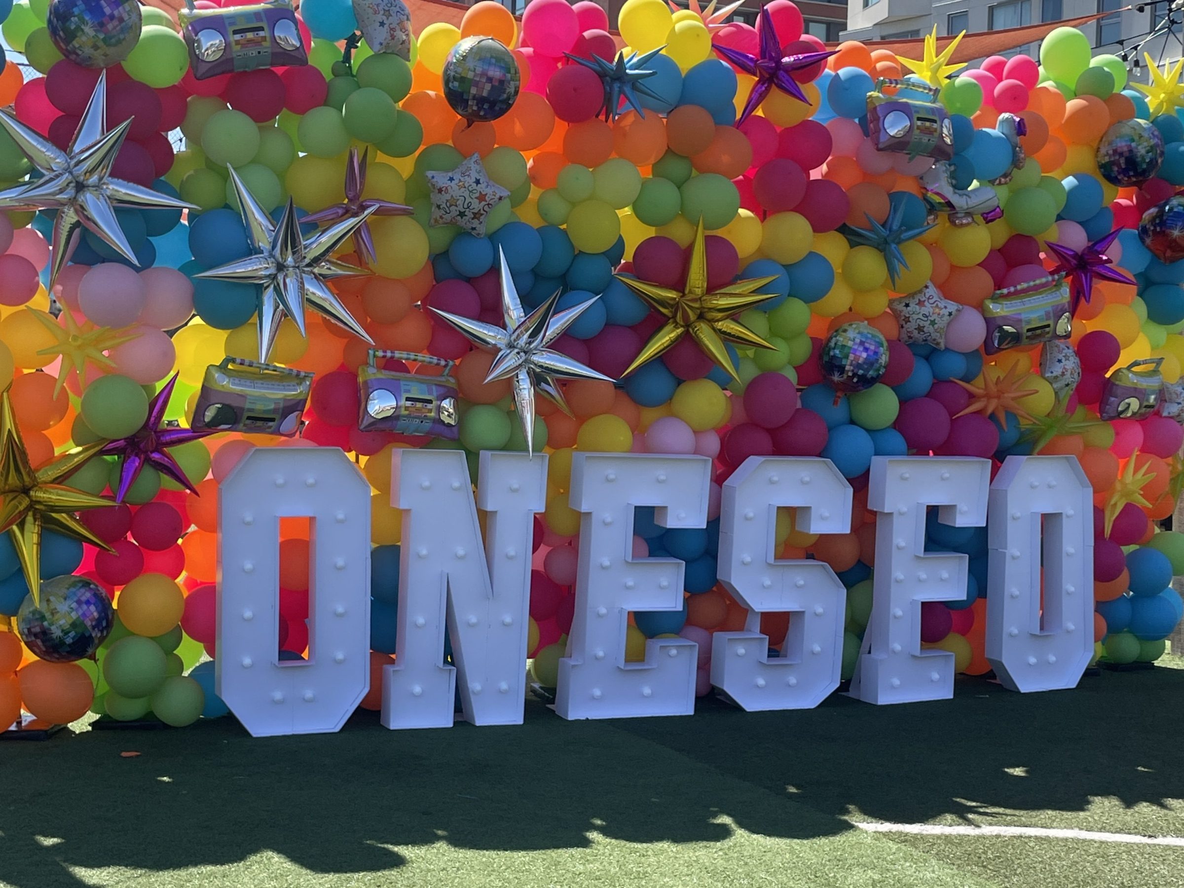 Colorful balloon backdrop with large letters spelling 'ONESE' outside.