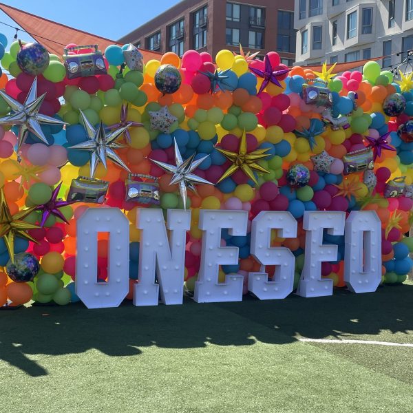 Colorful balloon backdrop with large letters spelling 'ONESE' outside.