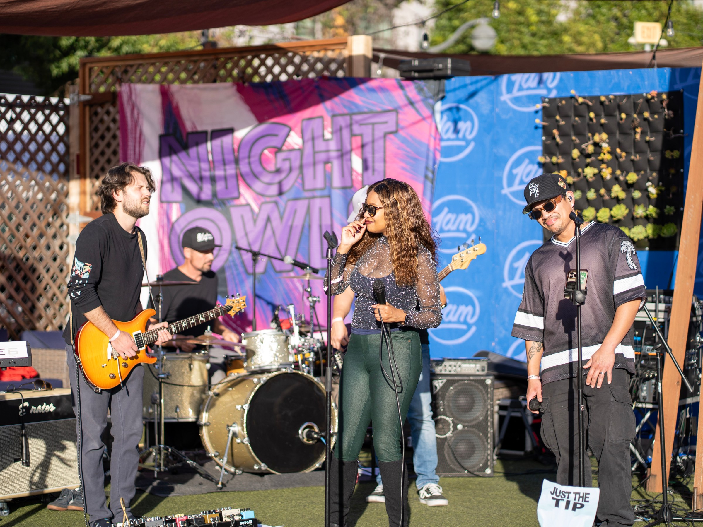 Band performing outdoors with banner reading 'Night Owl' in background.