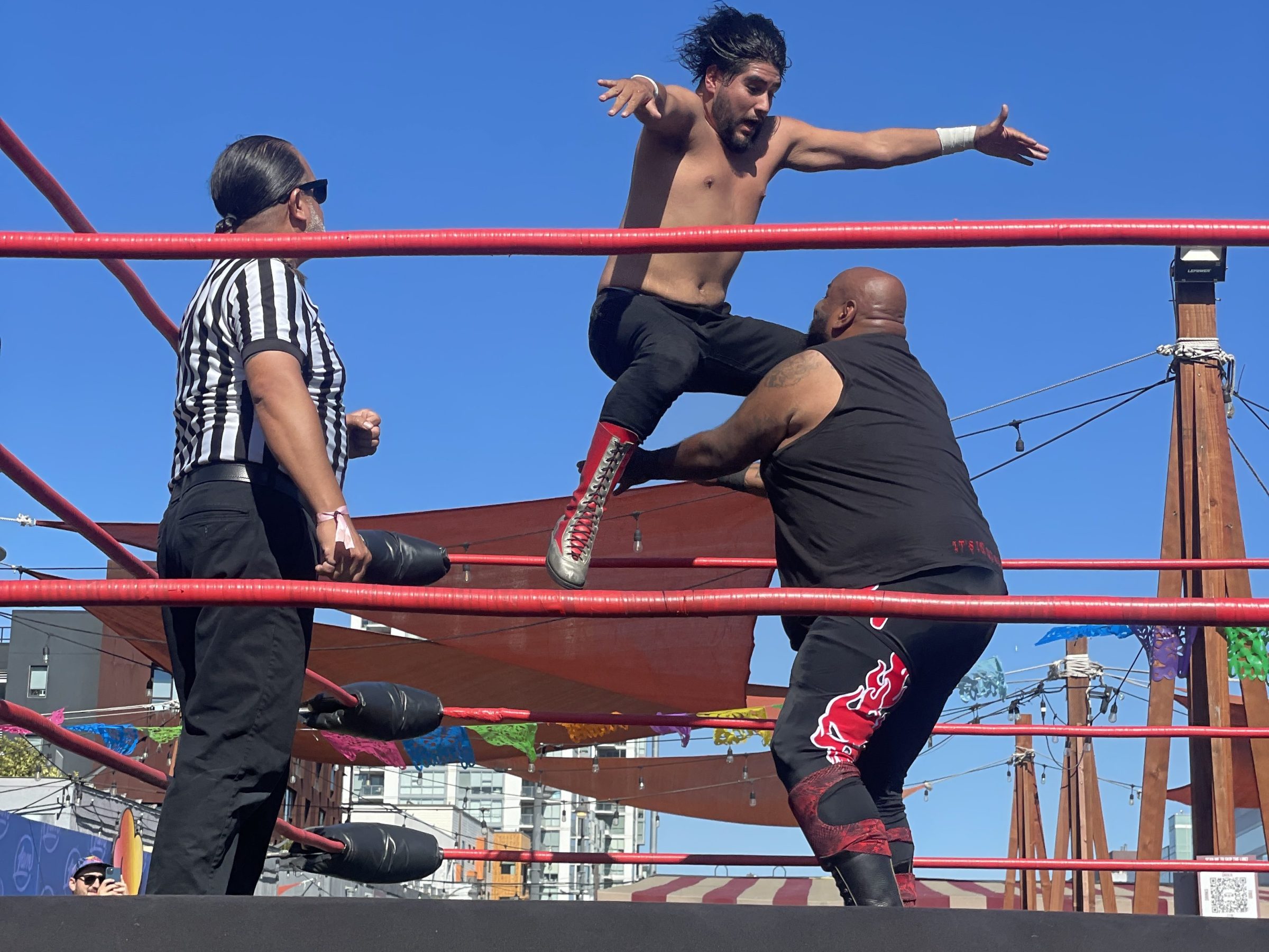 Wrestler in mid-air above opponent in a wrestling ring with referee nearby.