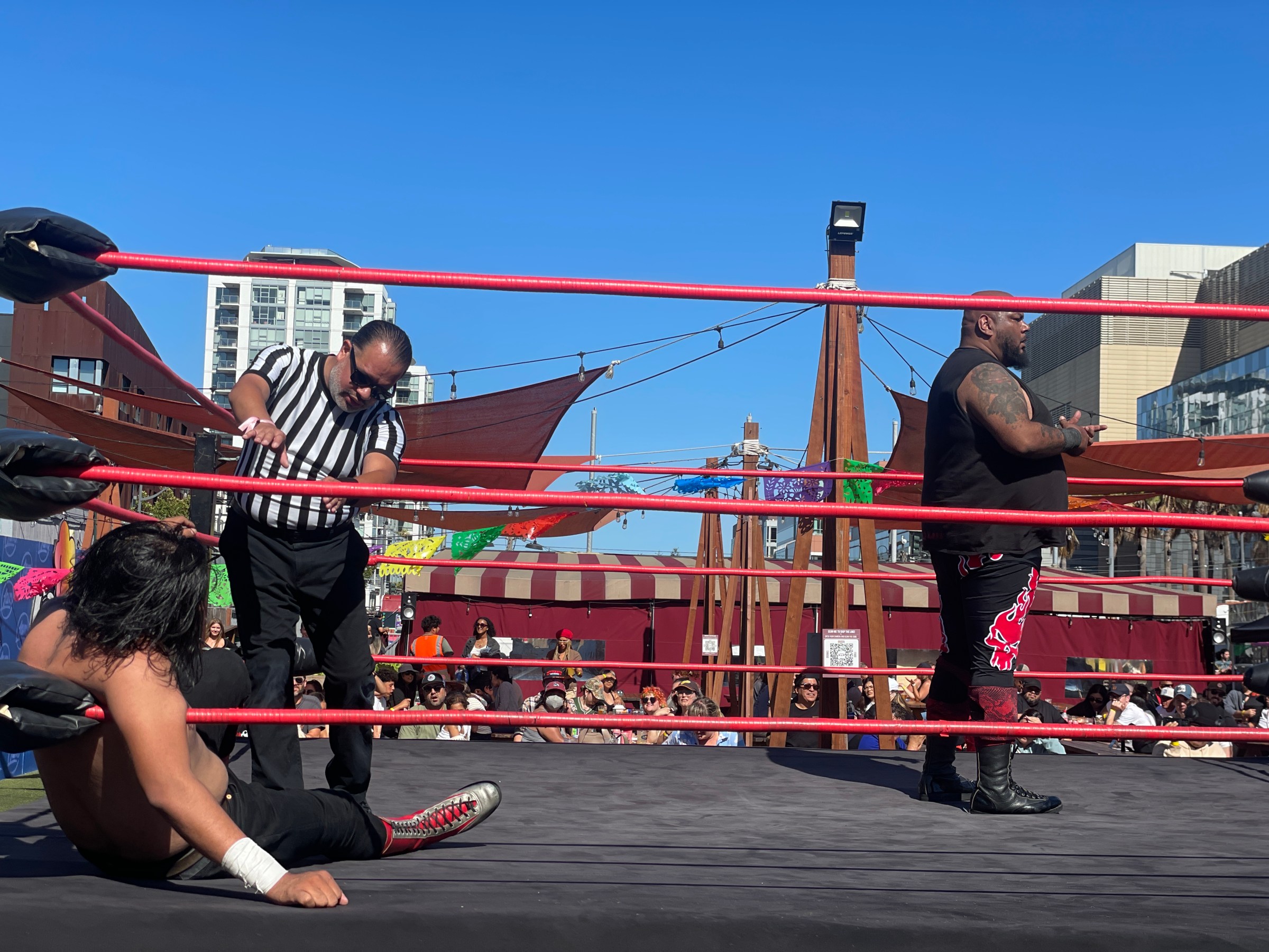 Wrestler stands in ring, another wrestler sits, referee checks the seated wrestler.