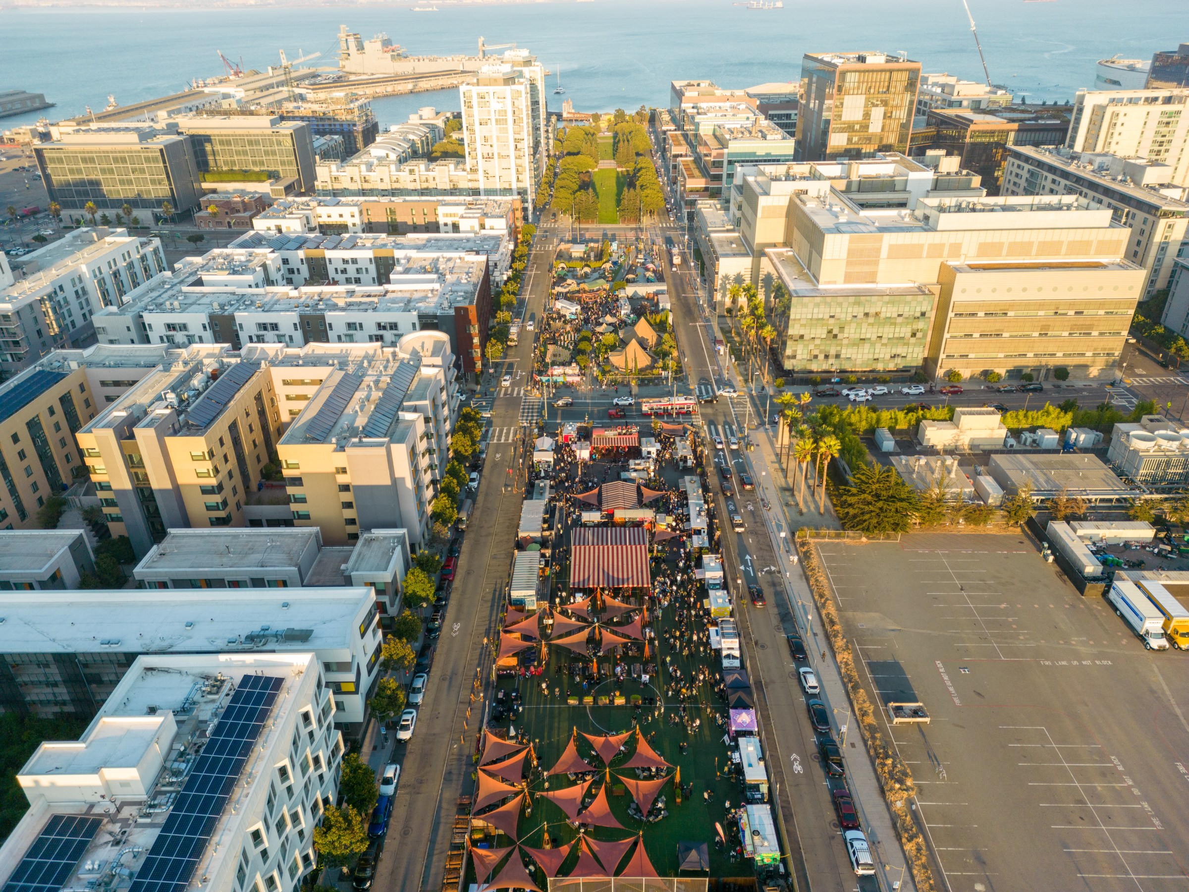 Aerial view of urban area with market tents and waterfront in the background.