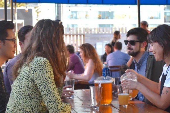 People sitting at a wooden table outdoors, enjoying drinks and talking.
