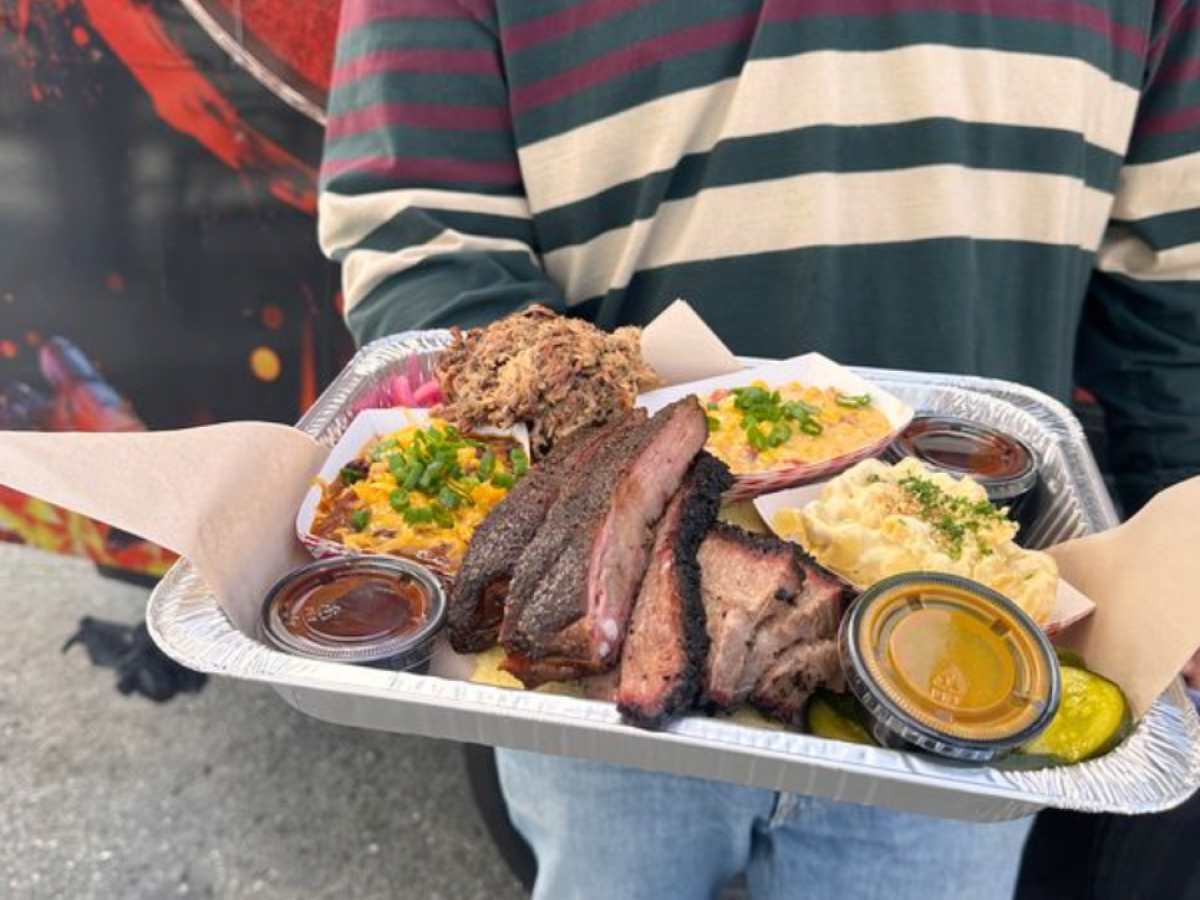 Person holding a tray of barbecue with sides outdoors.