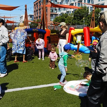 Children and adults at an outdoor event with inflatables and play equipment.