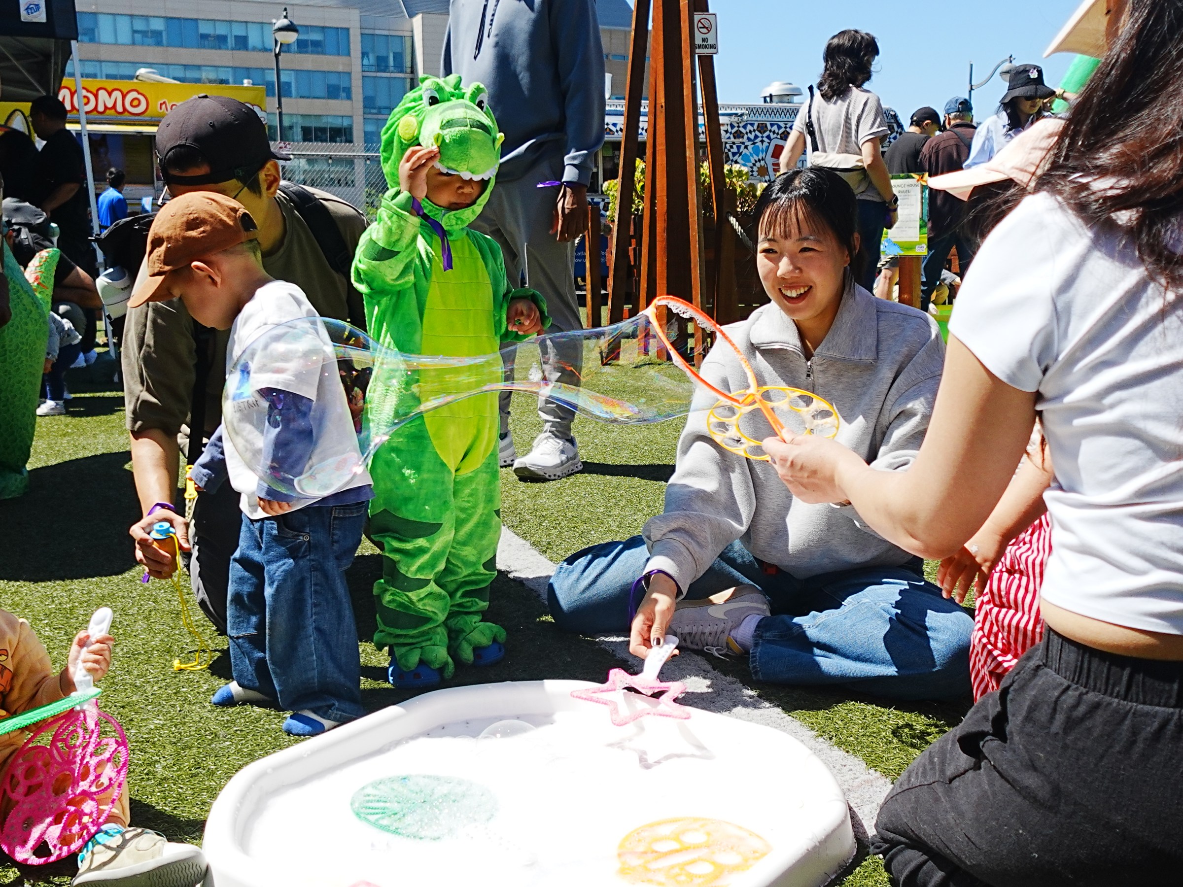 Children playing with bubbles outdoors, one dressed as a green dragon.