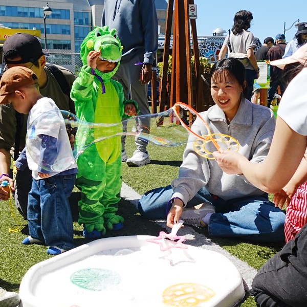 Children playing with bubbles outdoors, one dressed as a green dragon.