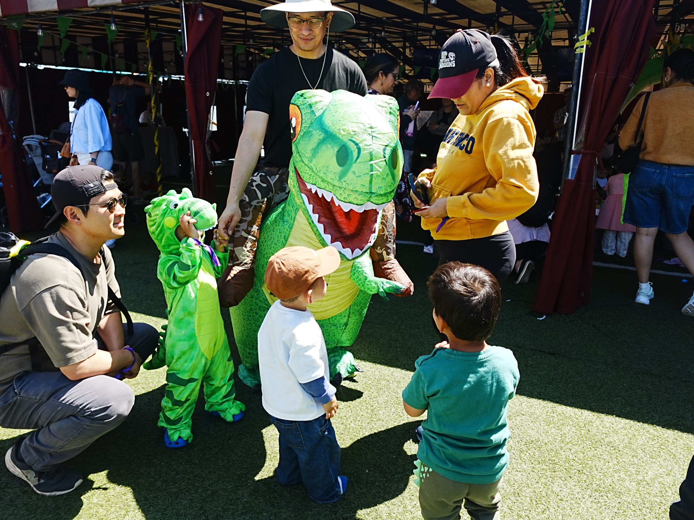 People and kids in dinosaur costumes interacting at an outdoor event.